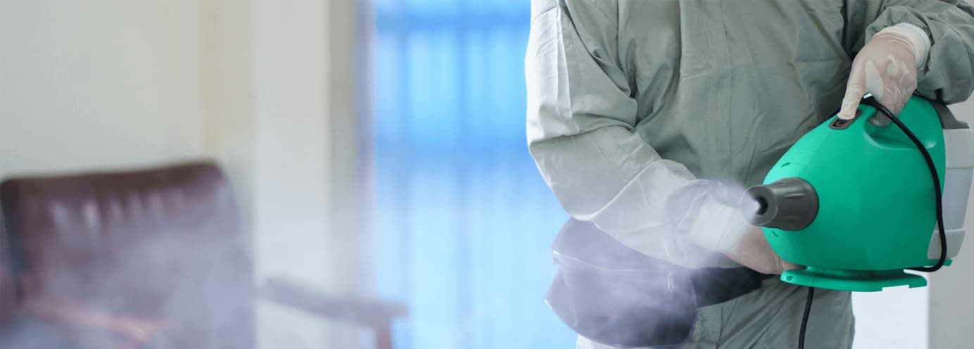 A professional cleaner in protective gear using a disinfectant fogger to sanitize a home interior